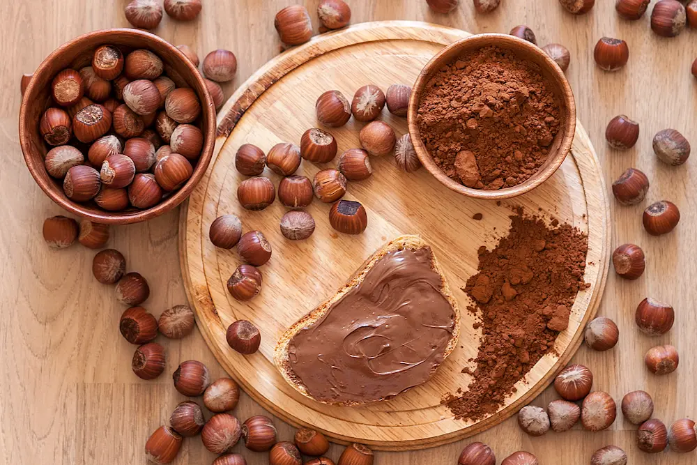Tagliere con nocciole, cacao e pane con crema di nocciole spalmata